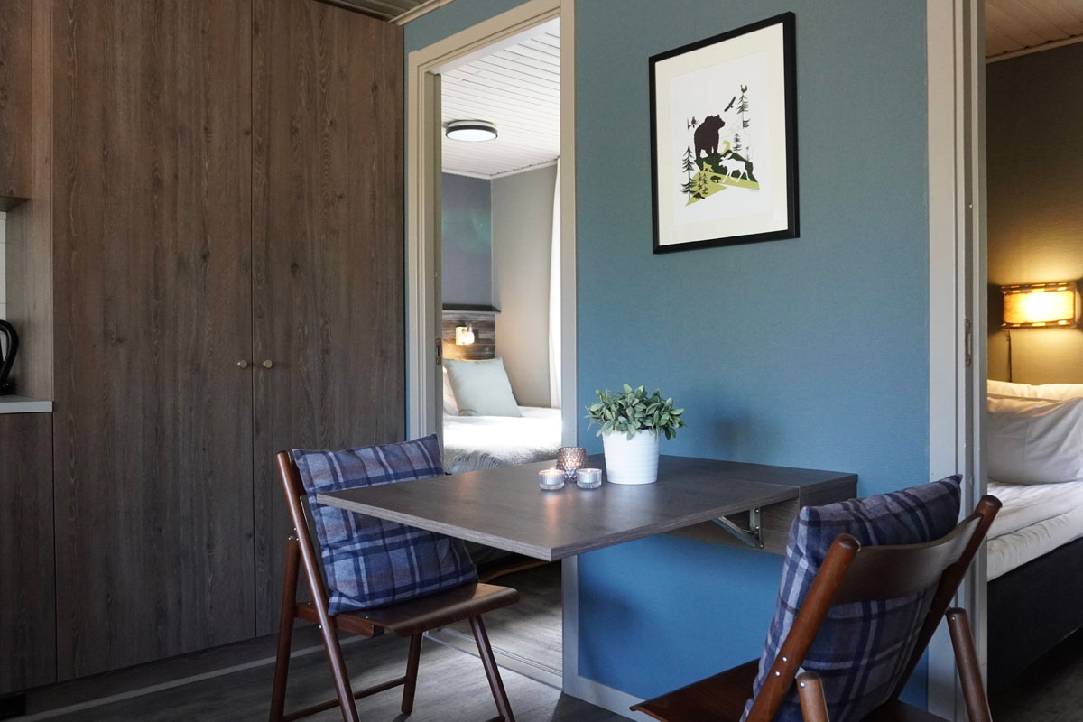 Living area and bedroom in a cabin at Brändön Lodge, with a folding table, Nordic decor, and a view into the second bedroom.