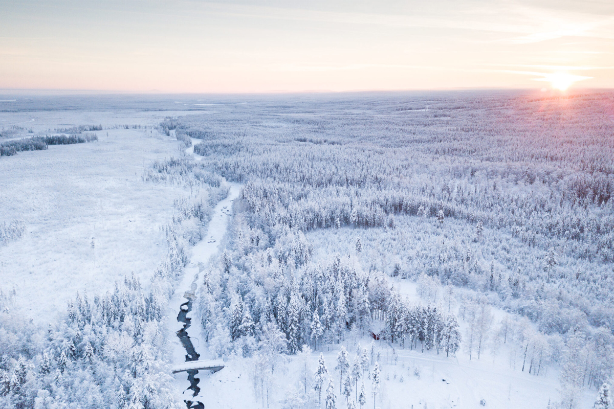 Aerial view of snow-covered forest and a frozen river near Loggers Lodge in Harads, Swedish Lapland.