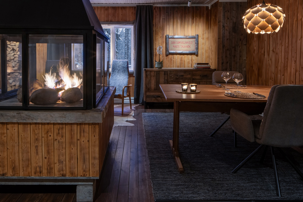 A cozy wood-paneled dining room with a central fireplace and set table at Loggers Lodge, Harads.