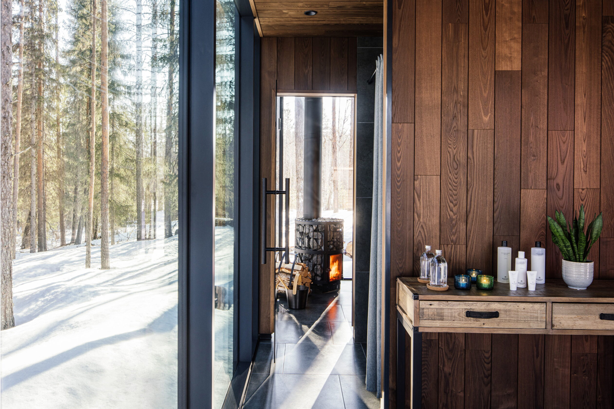A wood-paneled spa corridor at Loggers Lodge leads to a wood-burning stove, framed by forest views.