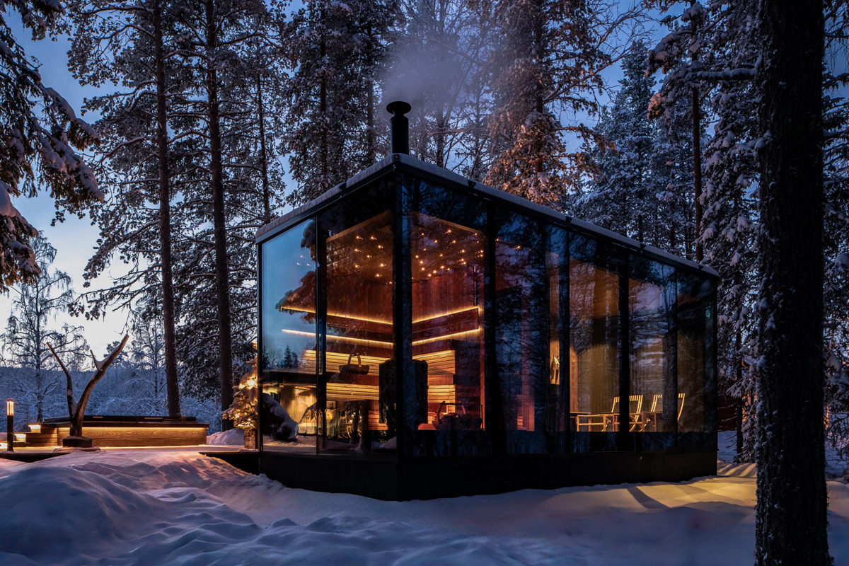 The glass-walled spa building glows warmly among snowy pines at Loggers Lodge, Harads, at dusk.