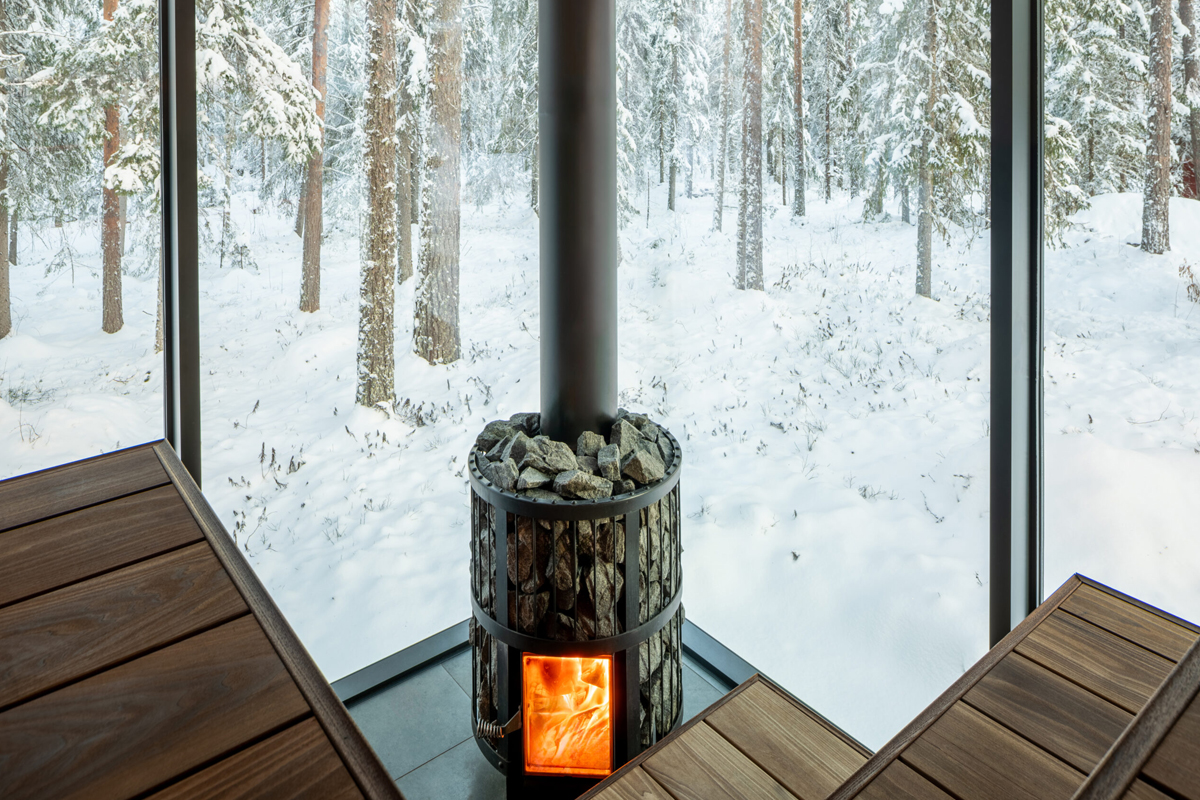A wood-fired sauna stove faces floor-to-ceiling windows overlooking snowy forest at Loggers Lodge.