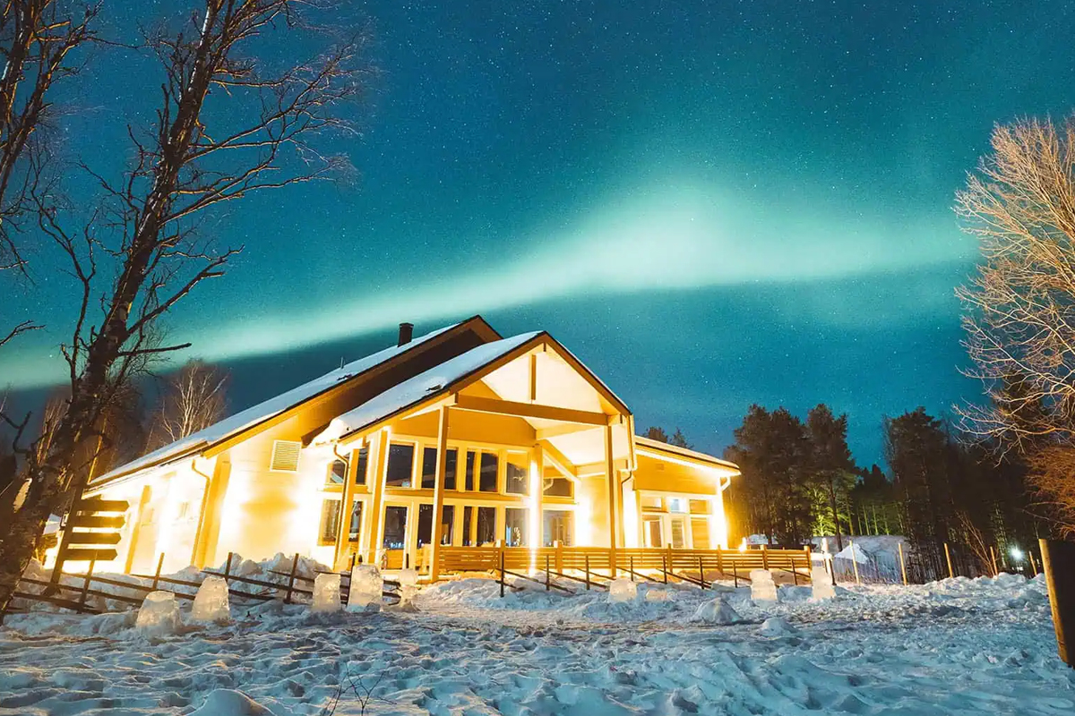 Restaurant Aitta at Apukka Resort glowing at night under the northern lights.