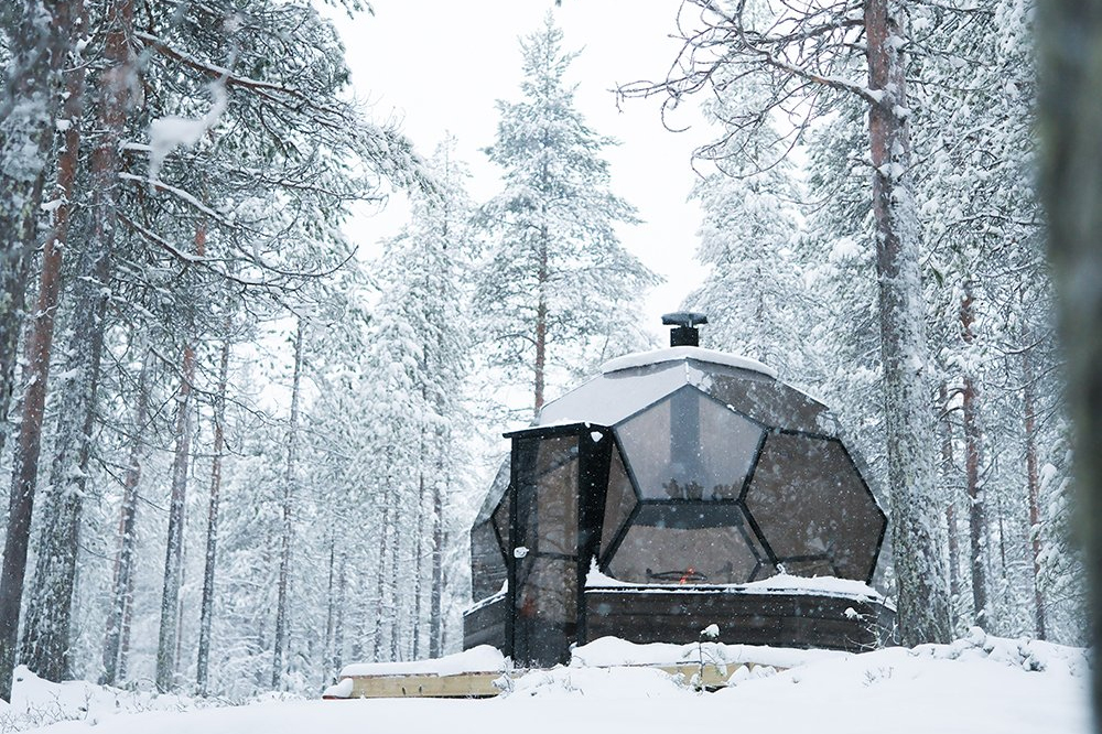 Glass kota igloo set among snow-covered trees during a snowfall, Halo Igloos, Rovaniemi