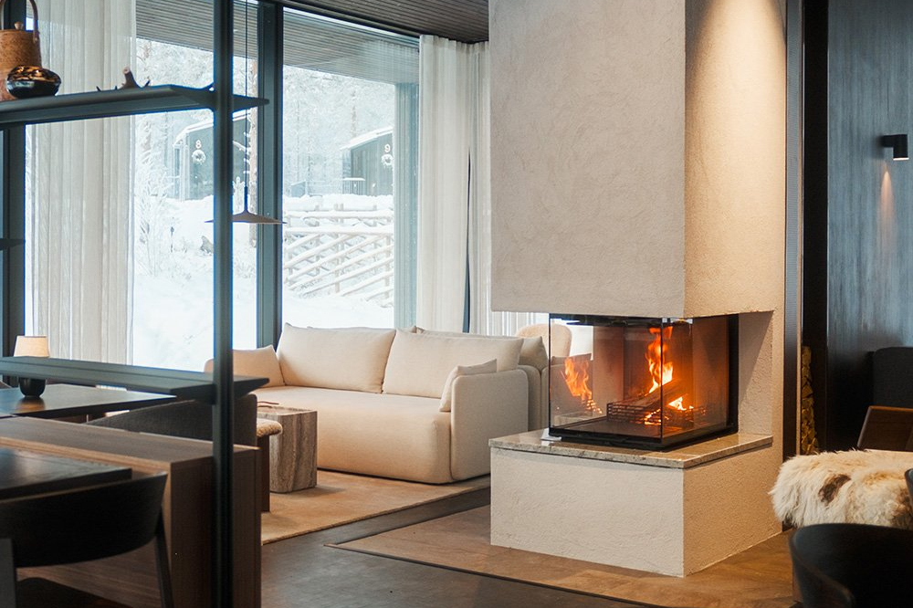 Igloo lounge at Halo with a lit fireplace, cream sofa and large windows overlooking a snowy forest, Rovaniemi