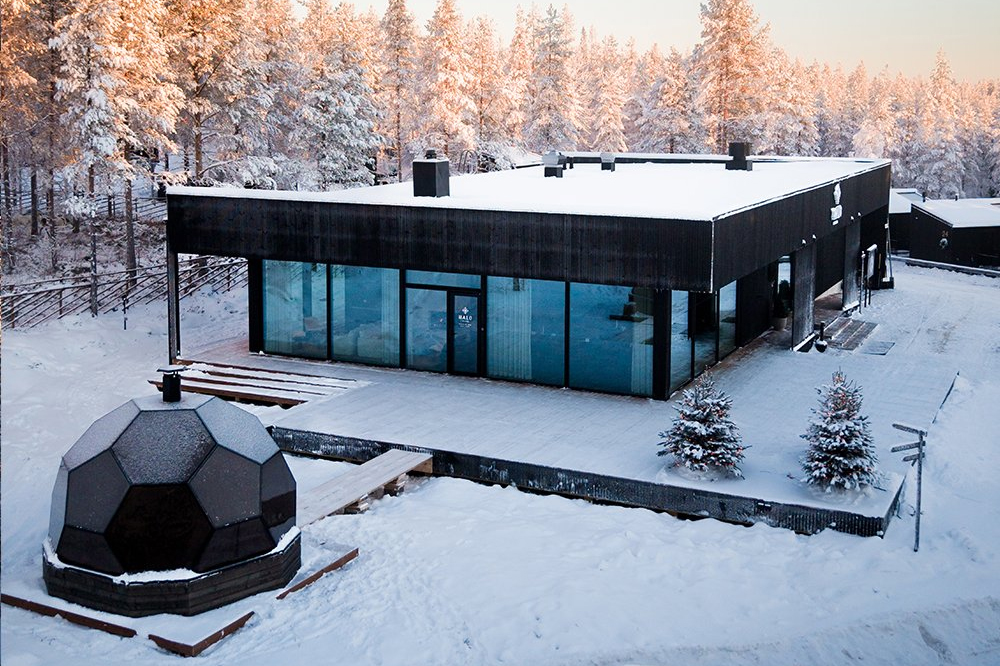 Halo Igloos main building with floor-to-ceiling glass facade and a glass kota in the foreground, Rovaniemi