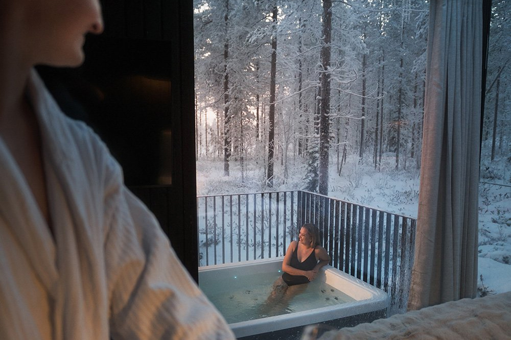 Guest relaxing in an outdoor jacuzzi on an igloo terrace overlooking a snow-covered forest, Halo Igloos, Rovaniemi