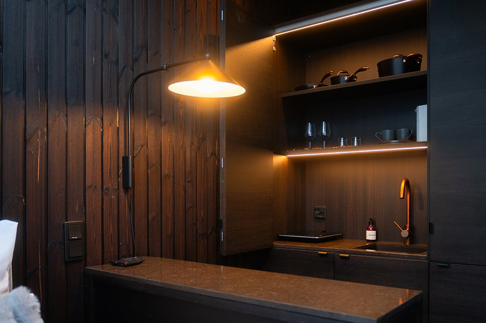 Dark wood igloo kitchenette with lit shelves, cookware, glassware and a copper tap, Halo Igloos, Rovaniemi
