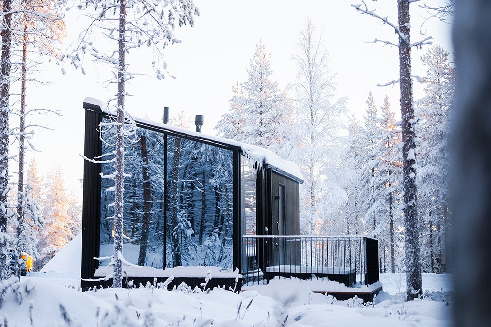 Dark glass-fronted igloo cabin with a private terrace set among snow-covered trees, Halo Igloos, Rovaniemi