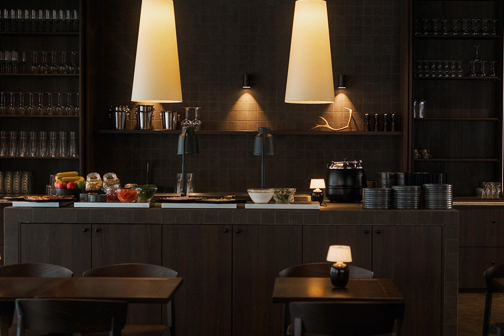 Dark restaurant buffet counter with warm pendant lights, glassware shelves and breakfast items, Halo Igloos, Rovaniemi