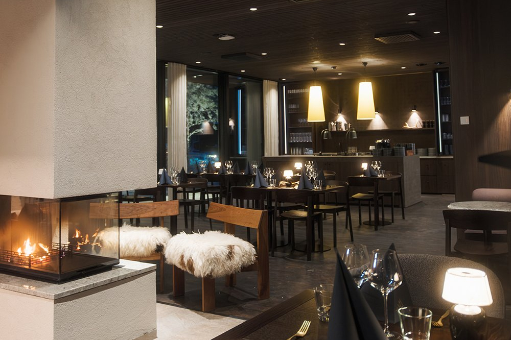 Restaurant dining room at Halo Igloos with a corner fireplace, fur stools, set tables and a bar area, Rovaniemi