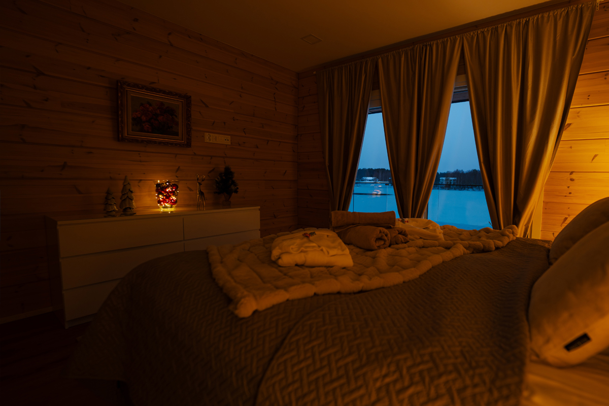 Chambre à la villa en soirée, peignoirs pliés sur le lit et vue sur le lac à travers les rideaux.