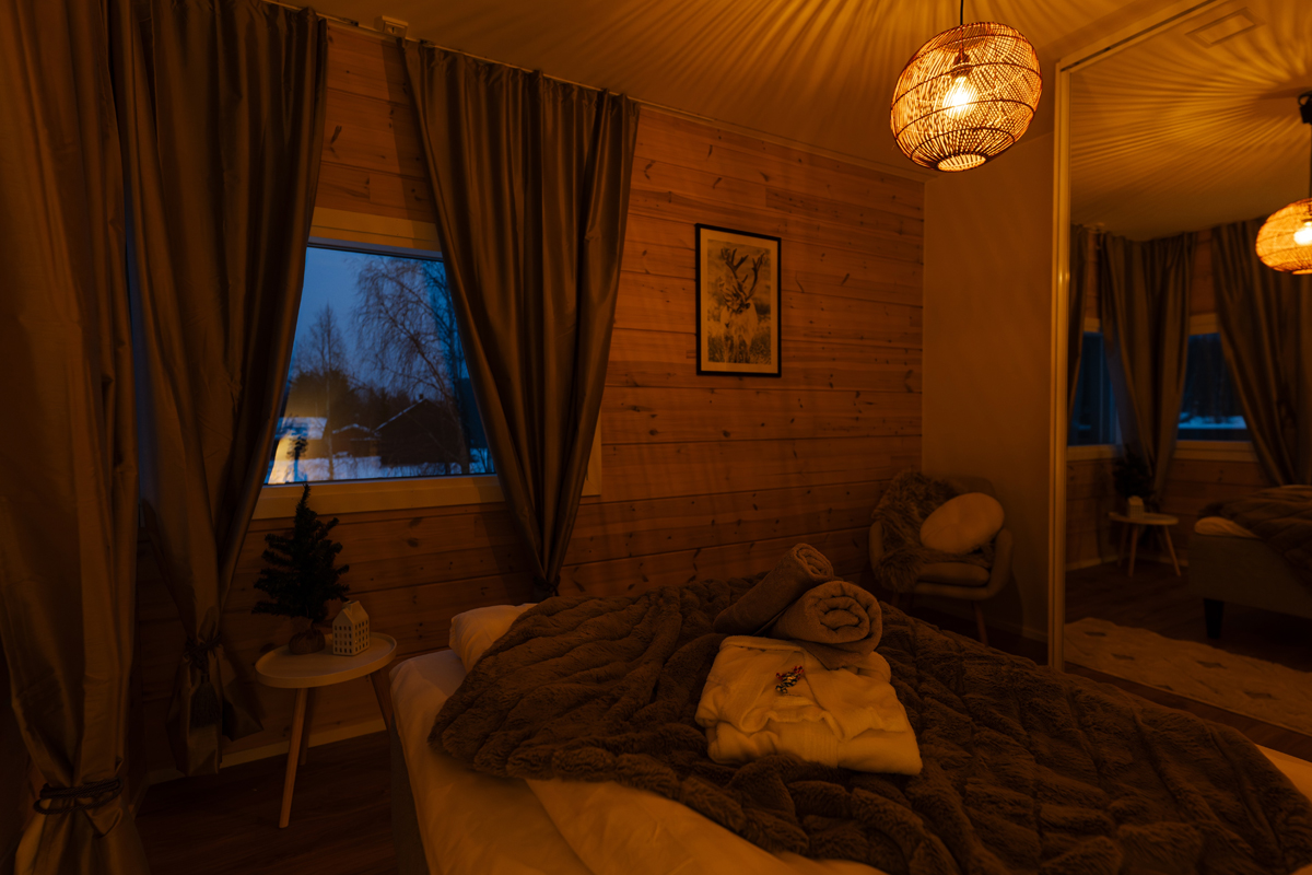 Chambre chaleureuse à la villa, éclairage doux, peignoirs et vue sur la forêt par la fenêtre.