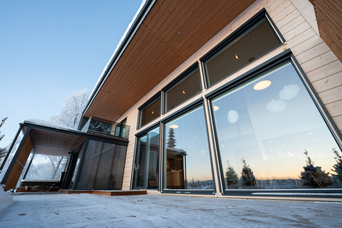 Vue extérieure de la façade vitrée de la villa reflétant le coucher de soleil hivernal.