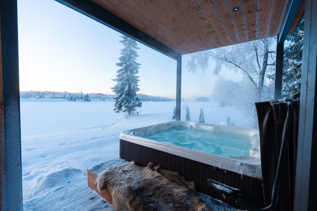 Jacuzzi extérieur à la villa de luxe au bord de la rivière, vue sur un lac enneigé et une peau de renne.