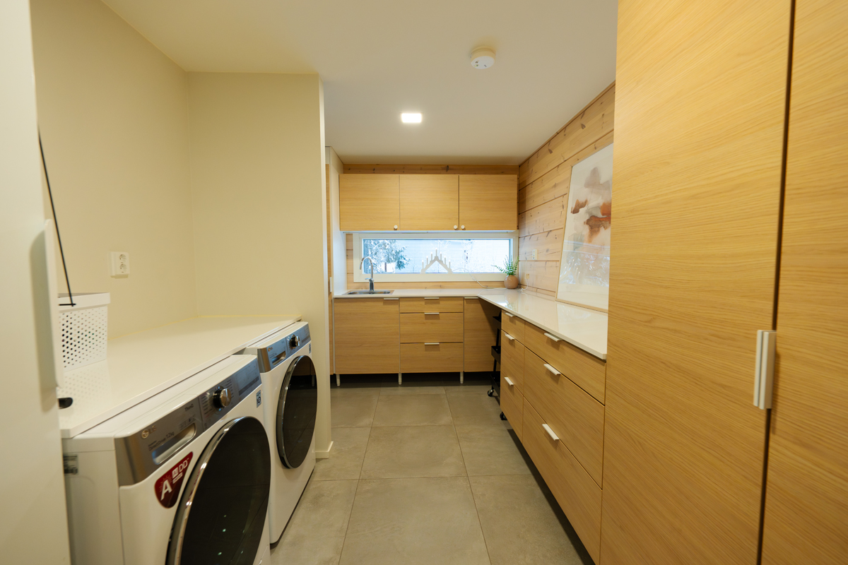 Buanderie de la villa avec lave-linge, sèche-linge et rangements en bois.
