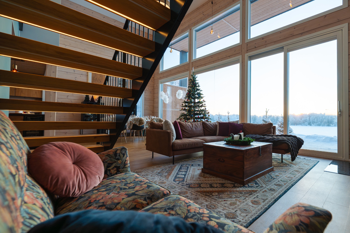 Salon de la villa avec fauteuils à motifs, poêle à bois et vue sur le lac.