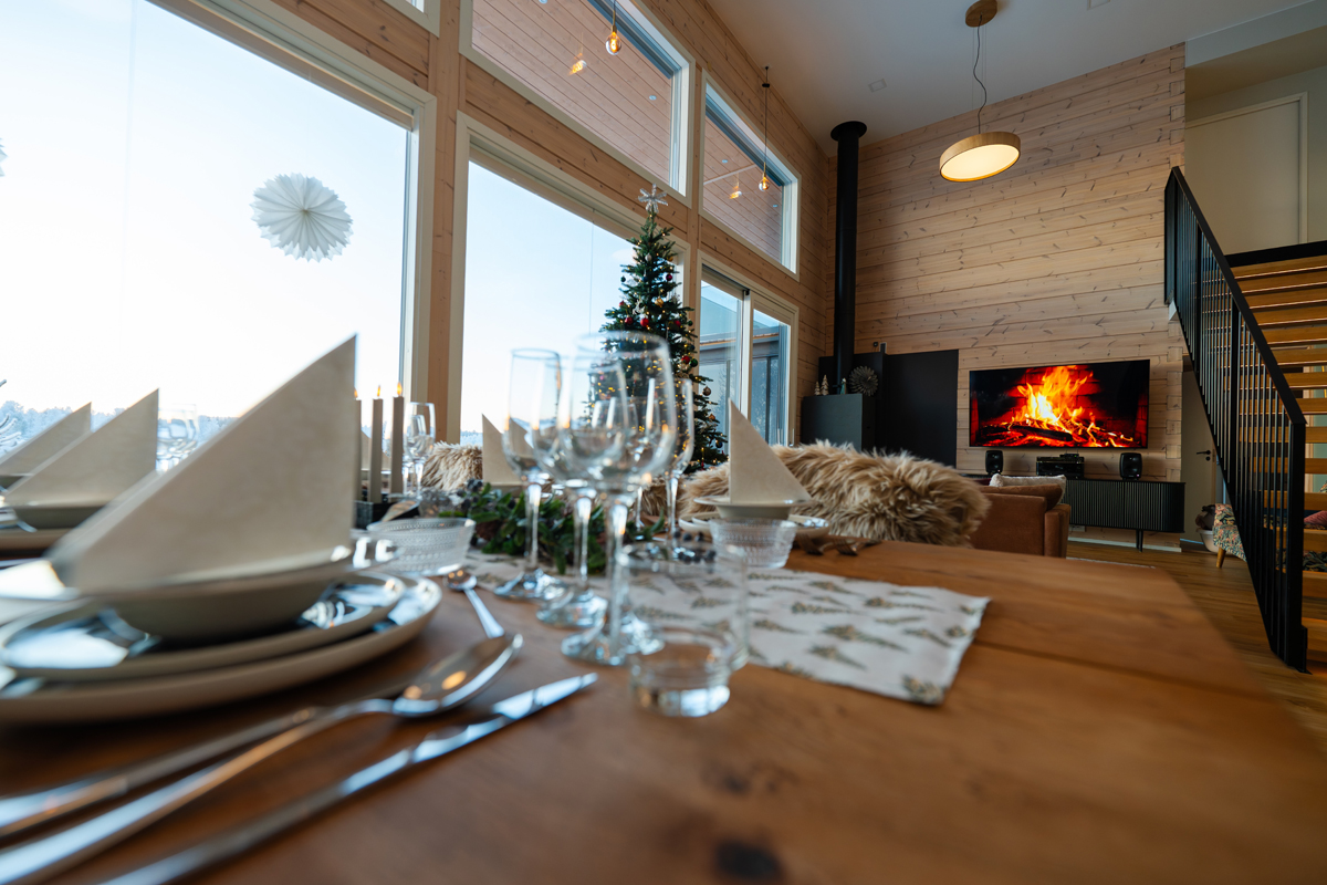Table dressée pour le dîner à la villa avec cheminée allumée et sapin de Noël en fond.
