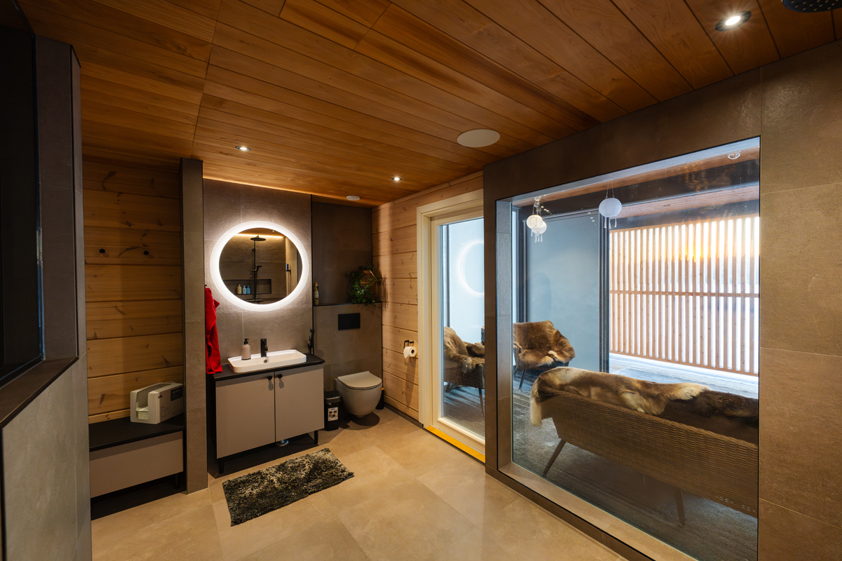 Salle de bain et coin salon de la suite sauna de la villa, vus à travers une cloison vitrée.
