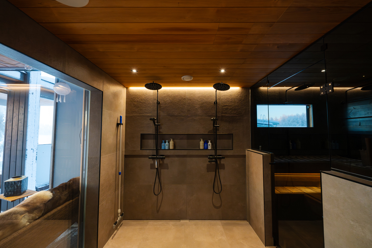 Douche à l'italienne dans la suite sauna de la villa, deux pommes de douche et vue sur la forêt.