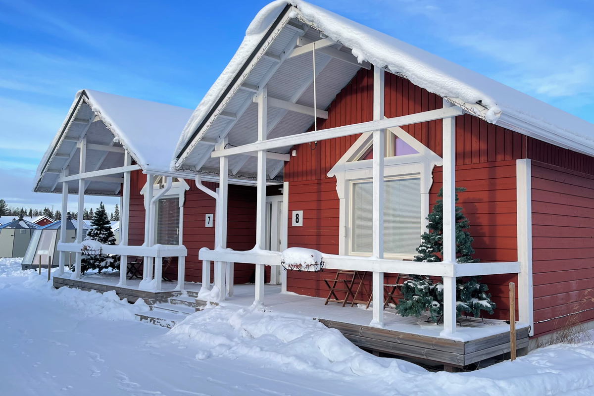 Red classic cottages lit with Christmas lights at night, with trees illuminated in purple and blue, Santa Claus Holiday Village, Rovaniemi