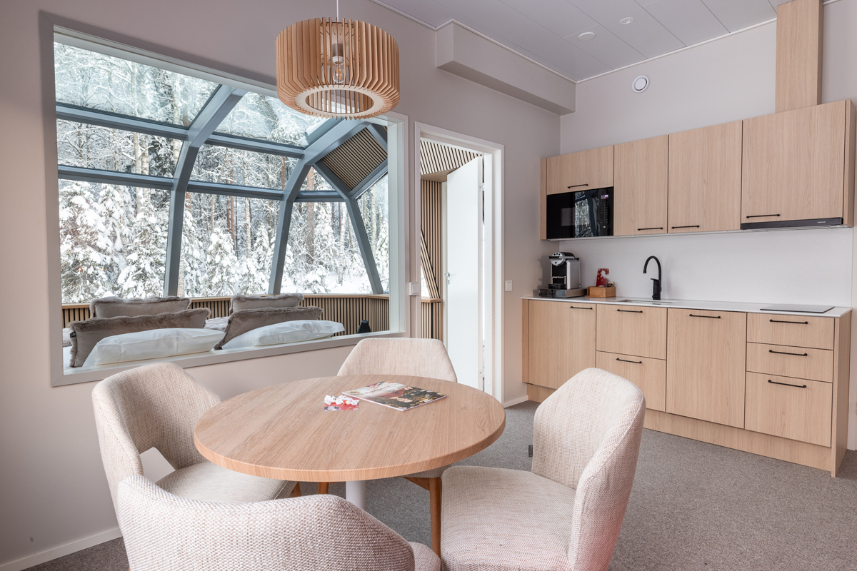 Kitchenette and dining area in a glass igloo cottage overlooking the glass sleeping pod and snowy forest, Rovaniemi