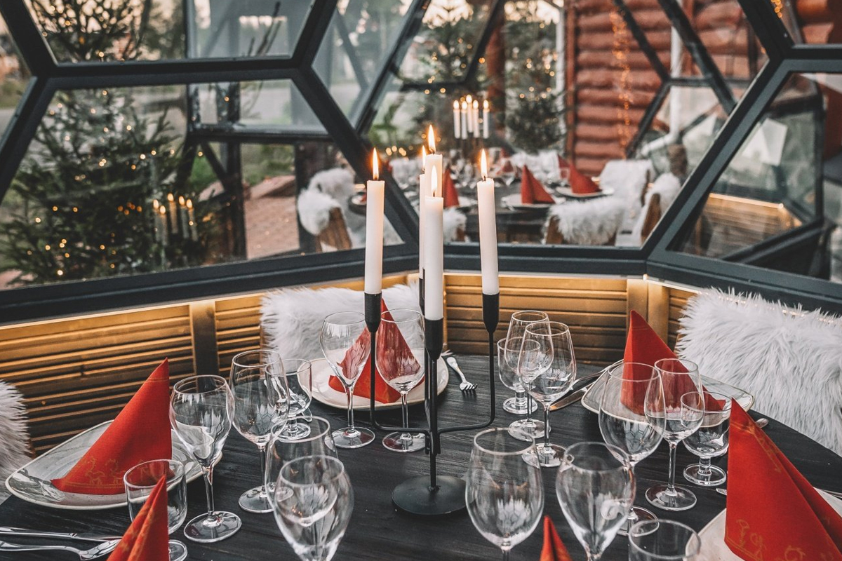 Candlelit table with red napkins inside a glass igloo, snowy forest visible through the panels, Rovaniemi