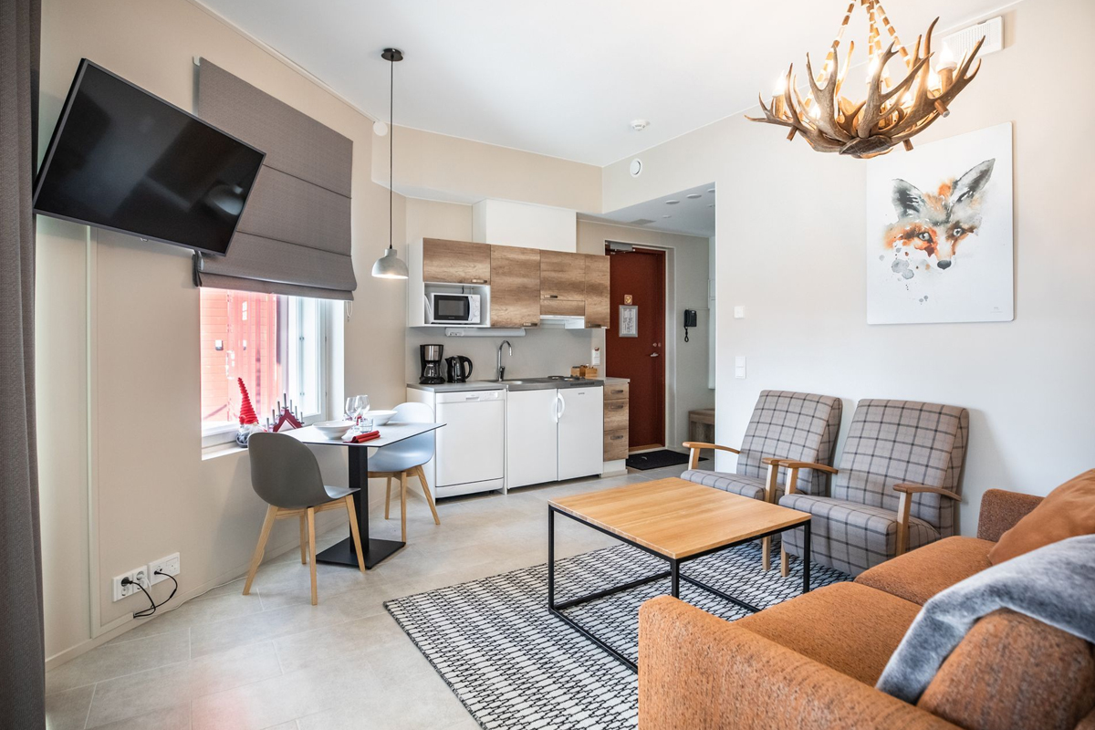 Open-plan living room and kitchenette of a Vispring suite with antler chandelier and fox artwork, Santa Claus Holiday Village, Rovaniemi
