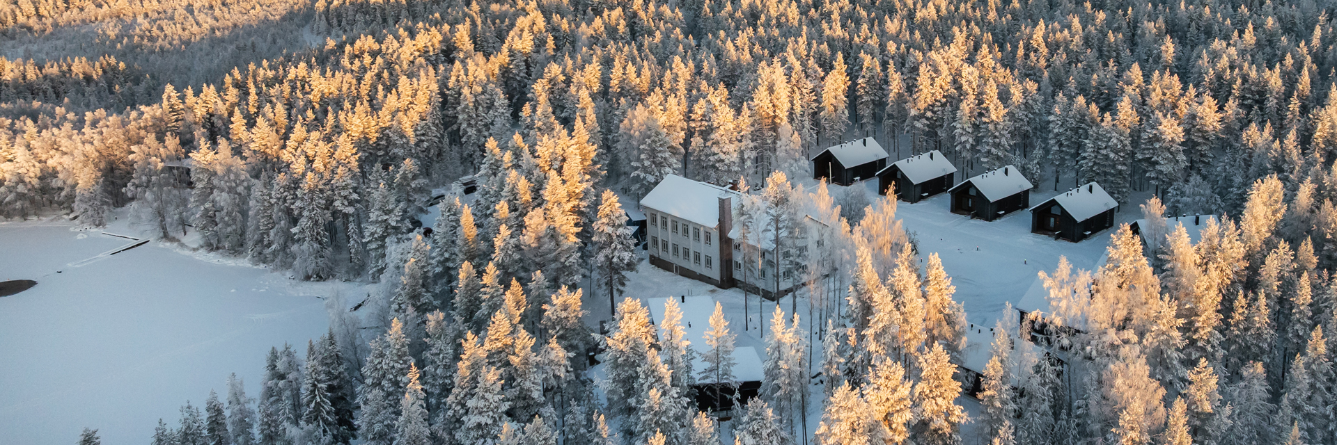 Aerial view of Skýra Retreat's main lodge and private cabins in a snowy forest near Rovaniemi.