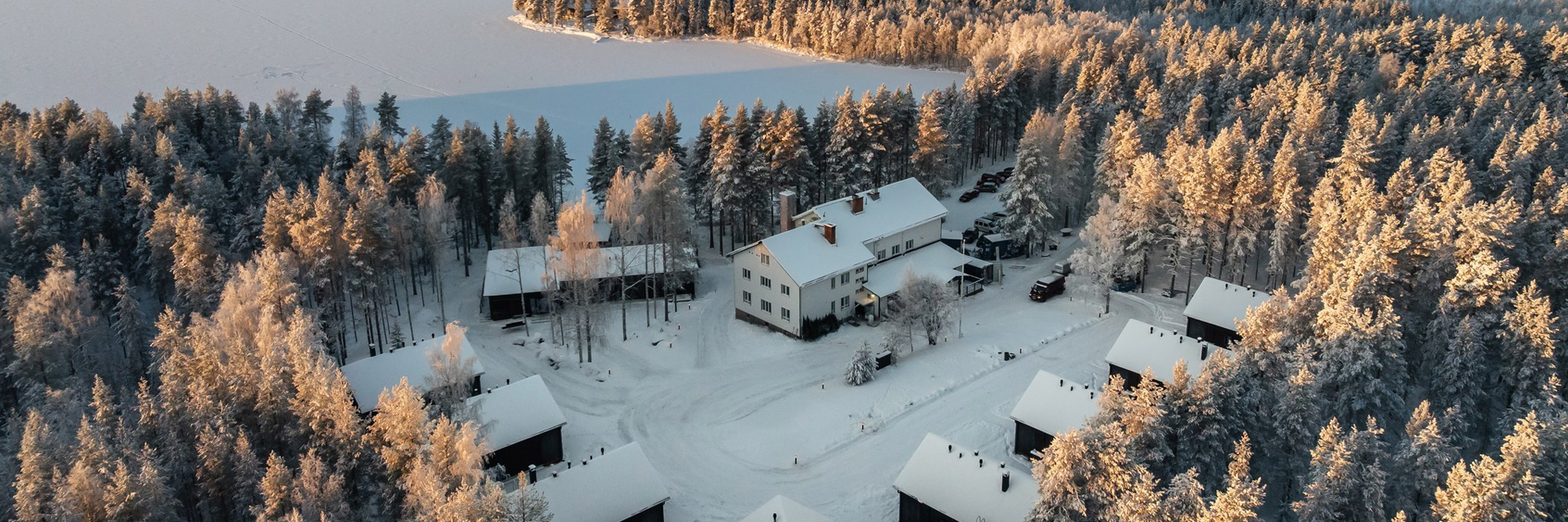 Vue aérienne du Skýra Retreat en hiver, entouré de forêts enneigées et du lac Norvajärvi gelé, près de Rovaniemi.