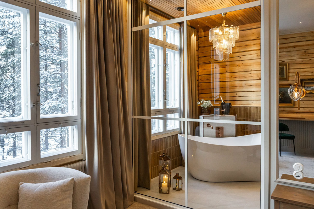 Baignoire îlot et sauna privé dans une Grande Suite du Skýra Retreat, avec vue sur la forêt à travers les fenêtres d'origine de l'ancienne école.