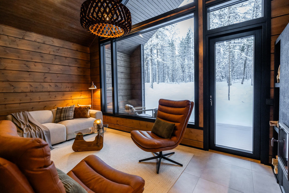 Salon d'un Log Suite au Skýra Retreat, avec fauteuils en cuir, murs en rondins et grandes fenêtres face à la forêt enneigée.