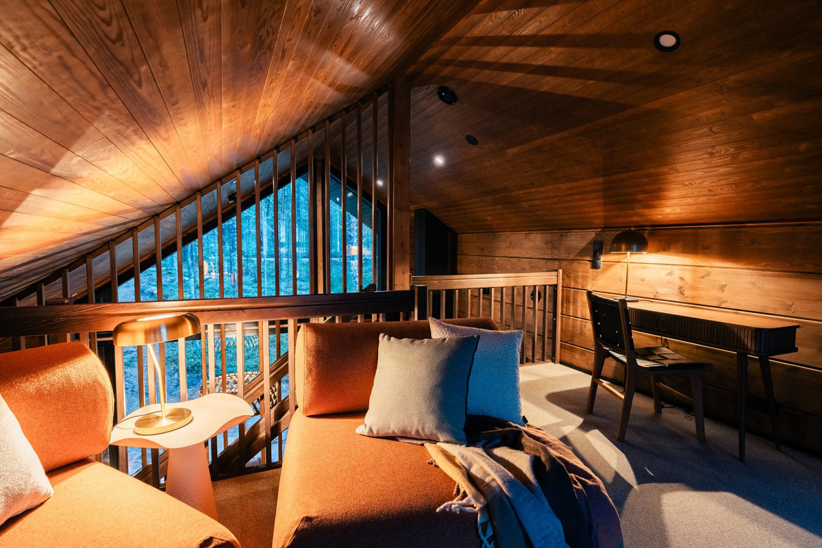 Espace mezzanine d'un Log Suite au Skýra Retreat, avec vue sur la forêt, bureau et coin salon chaleureux sous un plafond en bois.