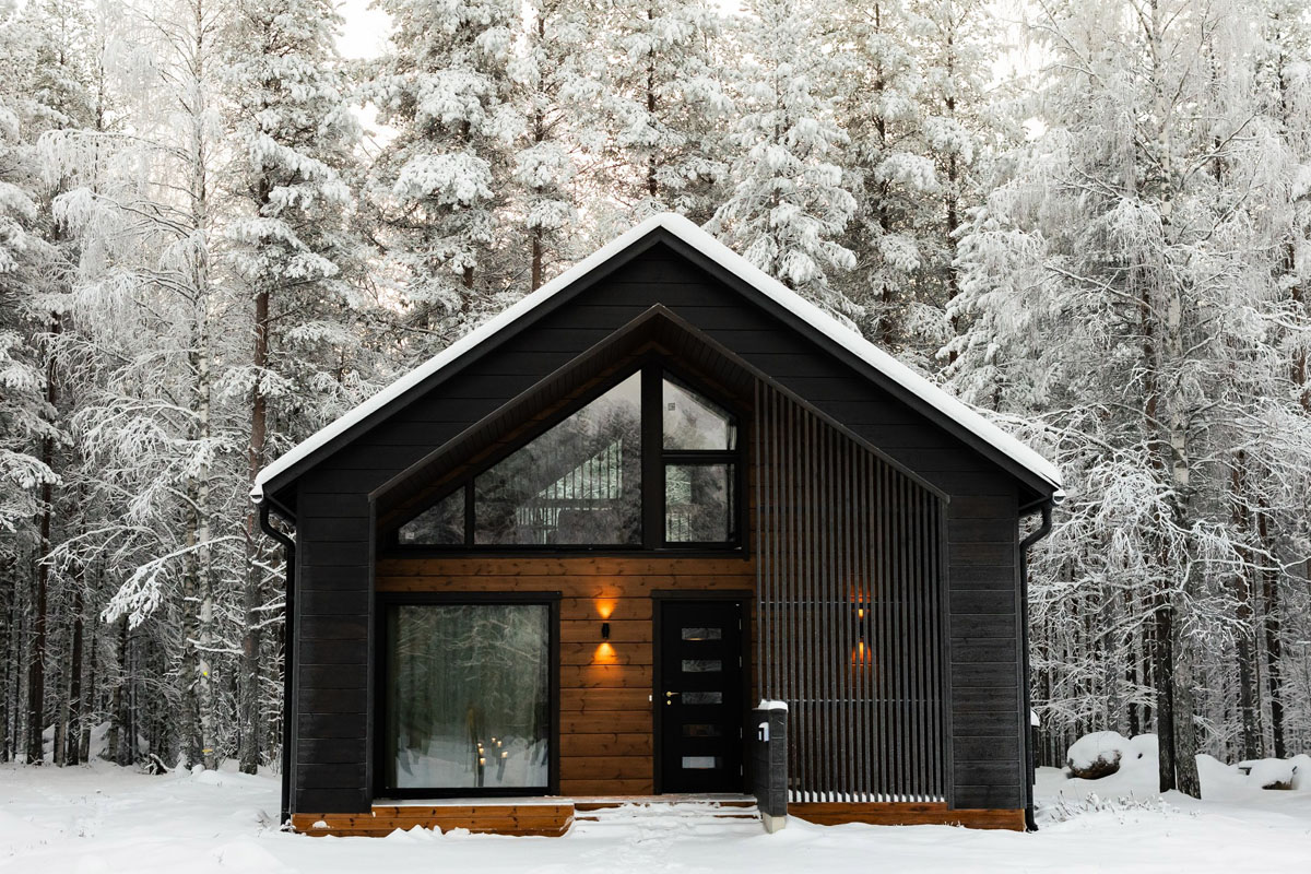 Extérieur d'un Log Suite du Skýra Retreat en hiver, avec de grandes fenêtres en pignon et une forêt enneigée tout autour.
