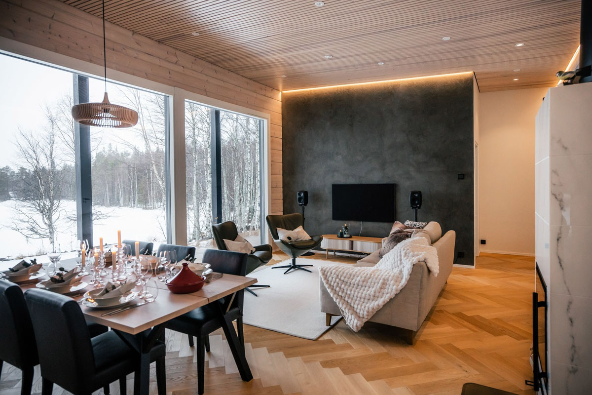 Espace séjour et salle à manger ouverts de la villa privée au bord du lac du Skýra Retreat, avec de grandes baies vitrées donnant sur un paysage hivernal enneigé.