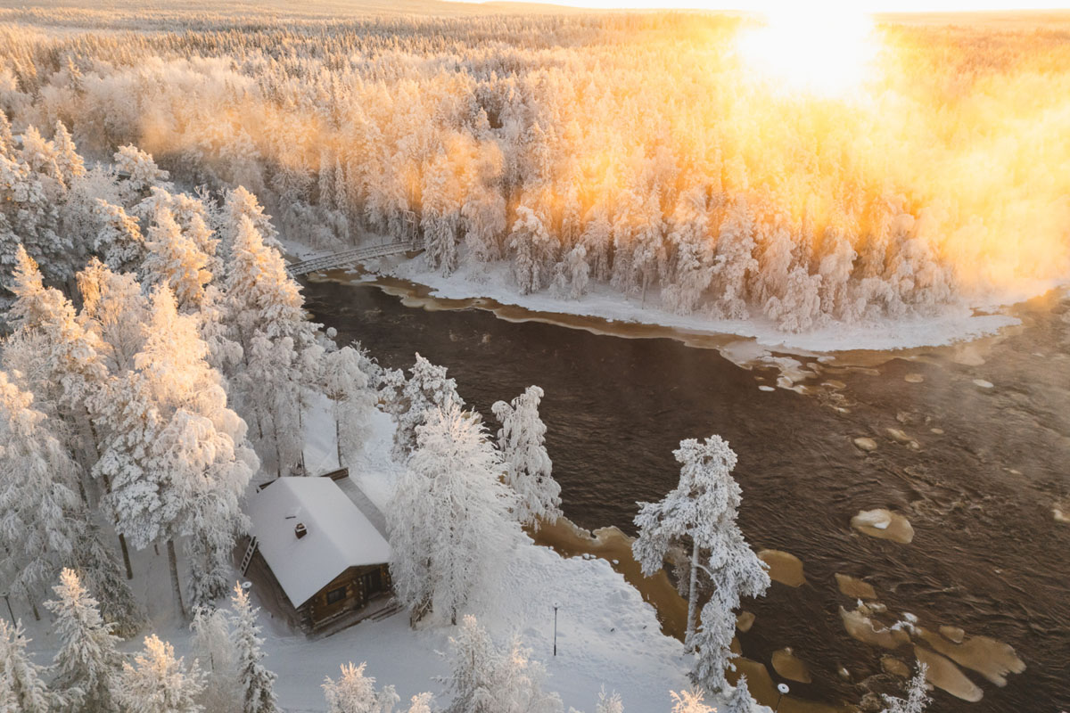 Vue aérienne d'une Riverside Suite du Vaattunki Wilderness Resort au bord de la rivière à l'heure dorée en hiver, près de Rovaniemi.