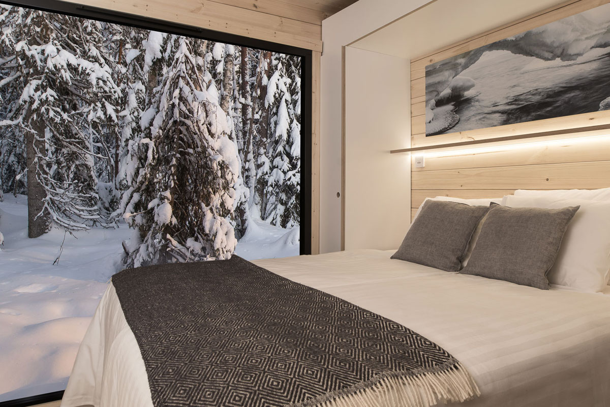 Chambre intérieure d'un Aurora Cabin Igloo au Vaattunki Wilderness Resort, avec une grande paroi vitrée face à la forêt enneigée.