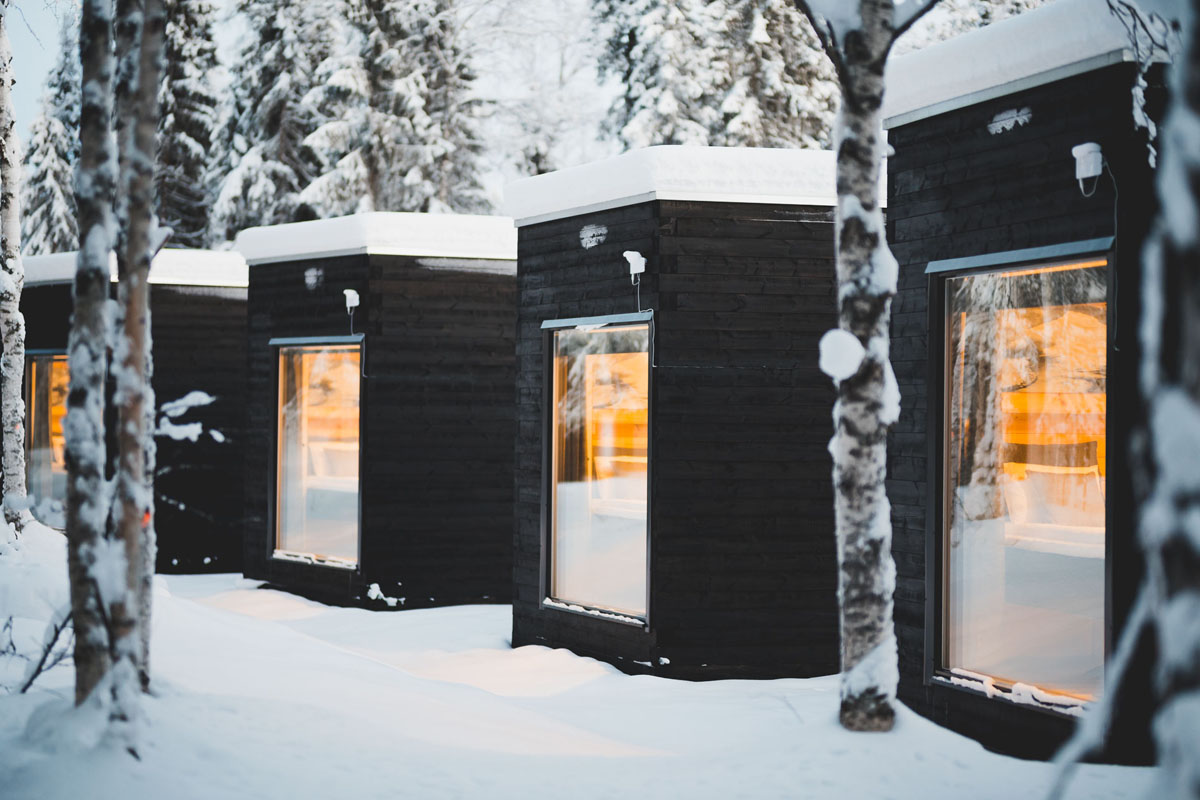 Rangée d'Aurora Cabin Igloos au Vaattunki Wilderness Resort en hiver, illuminés chaleureusement parmi les bouleaux enneigés près de Rovaniemi.