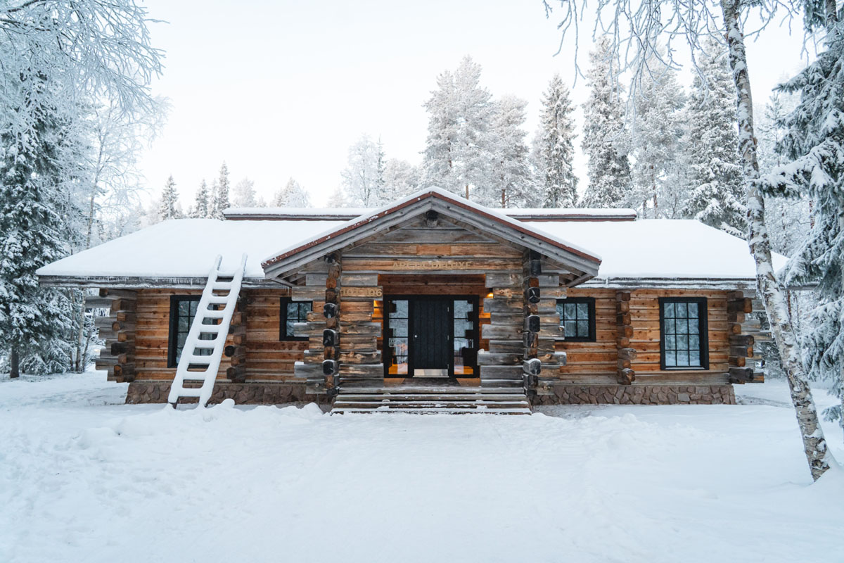 Extérieur d'un chalet en rondins Arctic Deluxe au Vaattunki Wilderness Resort en hiver, entouré de bouleaux enneigés près de Rovaniemi.