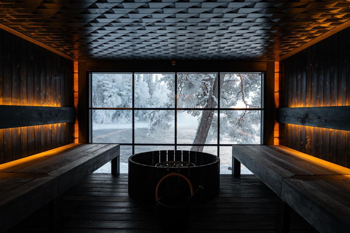 Intérieur du sauna du Vaattunki Wilderness Resort, avec des bancs en bois sombre et une grande baie vitrée donnant sur un paysage hivernal enneigé.