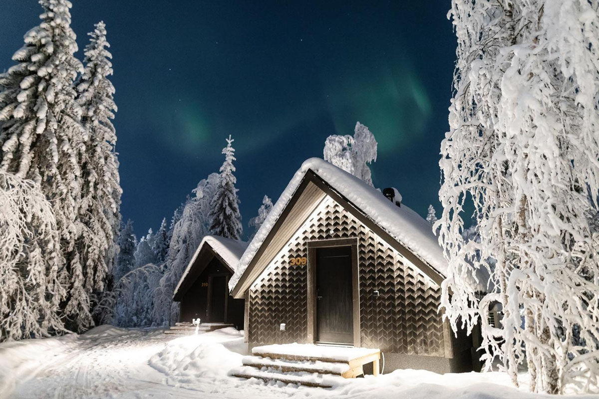 Chalets Panorama Hut du Vaattunki Wilderness Resort de nuit, avec les aurores boréales au-dessus de la forêt enneigée près de Rovaniemi.