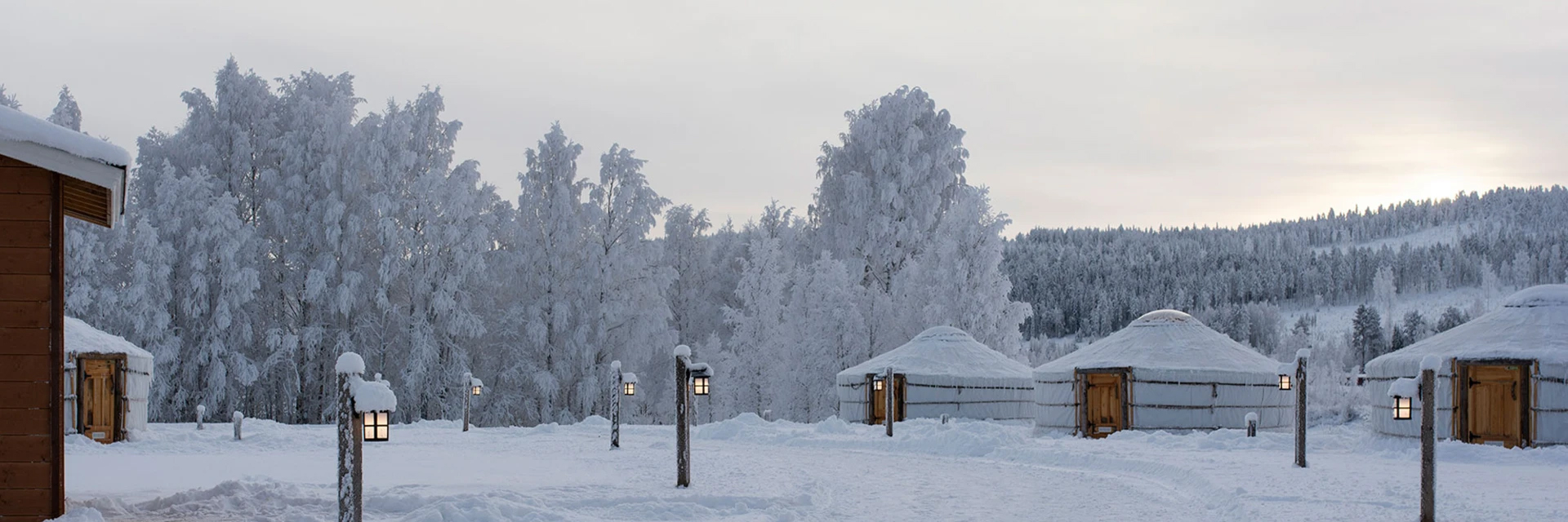Snow covered yurts at Yurt District in Rovaniemi, lit lanterns lining a path through frosted trees.