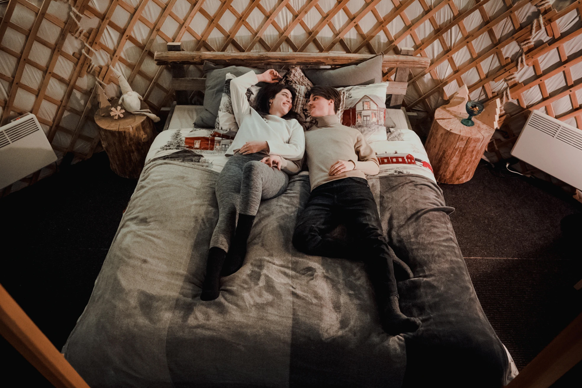 A couple relaxes together on the bed inside a yurt at Yurt District.