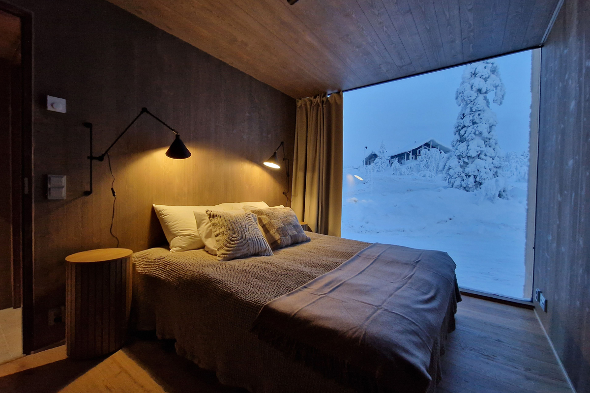 Dimly lit double bedroom with floor-to-ceiling window revealing a snow-covered evening landscape outside