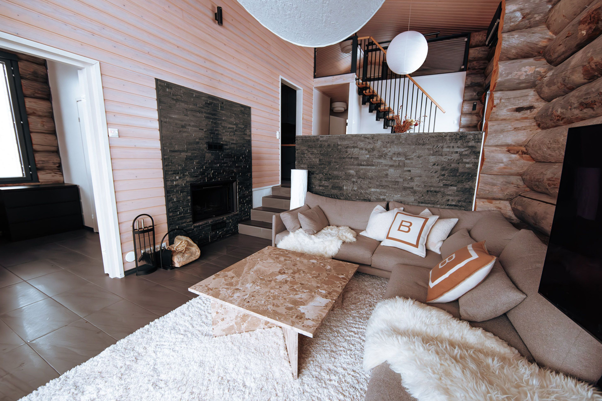 Spacious log cabin living room with a stone fireplace, large marble coffee table, sheepskin throws, and mezzanine staircase