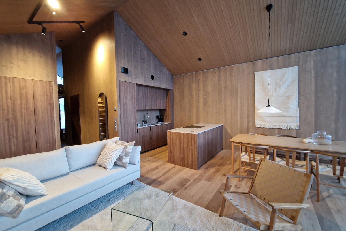 Open-plan cabin kitchen and living area with dark walnut cabinetry, a kitchen island, and Scandinavian dining furniture