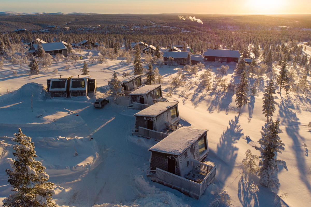 Aerial view of Aurora Collection cabins set in a snow-covered boreal forest at golden hour, Saariselkä