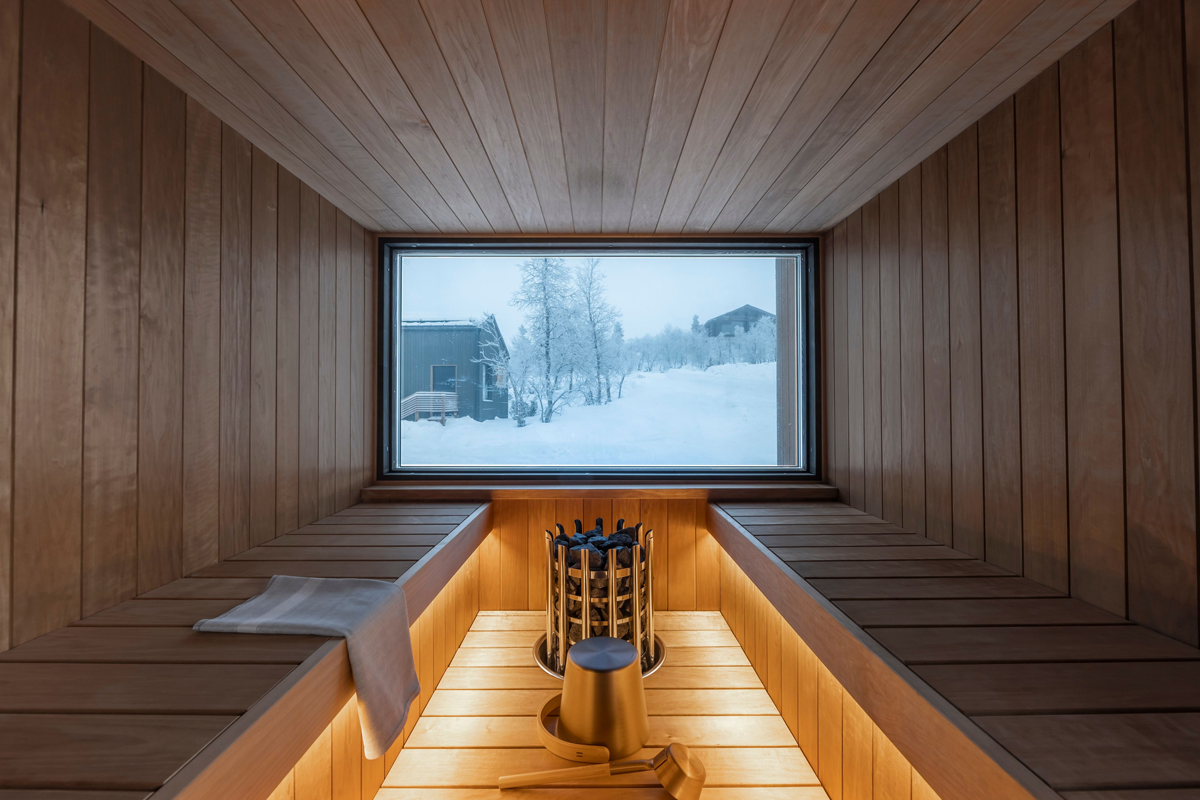Finnish sauna interior with warm wood paneling, bench lighting, and a window looking onto a snowy winter scene