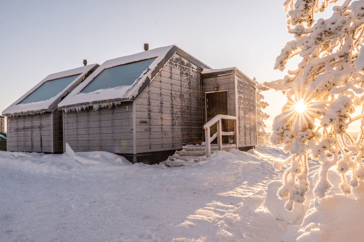 Frost-covered Aurora Collection cabin in deep winter sunlight, surrounded by snow-laden pine trees, Saariselkä