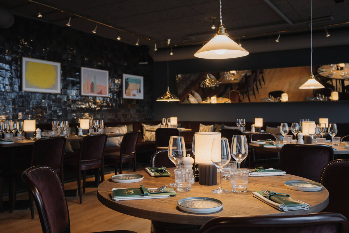 Interior of restaurant NÒR Södermalm at Clarion Hotel Stockholm, with round tables, velvet chairs, warm lighting, and Scandinavian artwork.